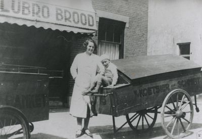 875156 Portret van mevr. Roks met haar zoontje Cor bij twee broodkarren voor het filiaal van de Lubro-bakkerij ...